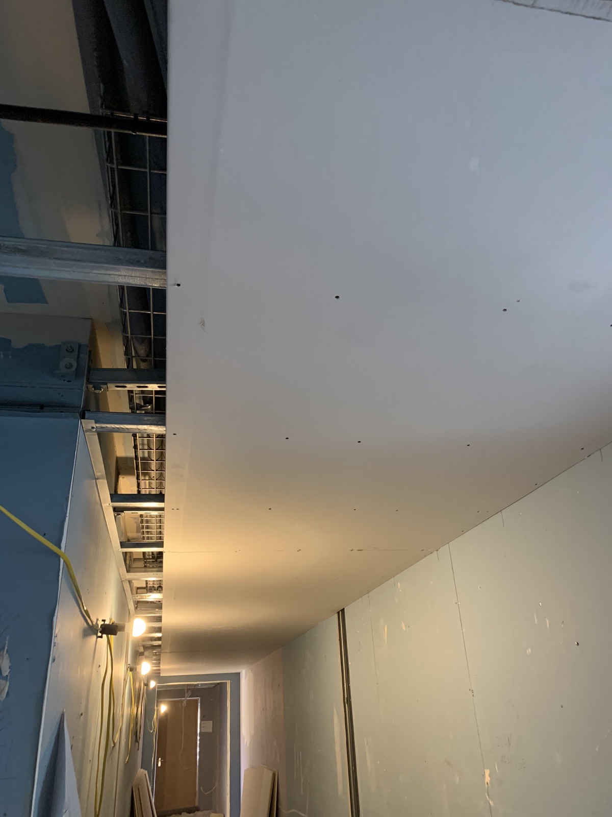 Plasterboard fixed to the new MF ceiling along a commercial corridor